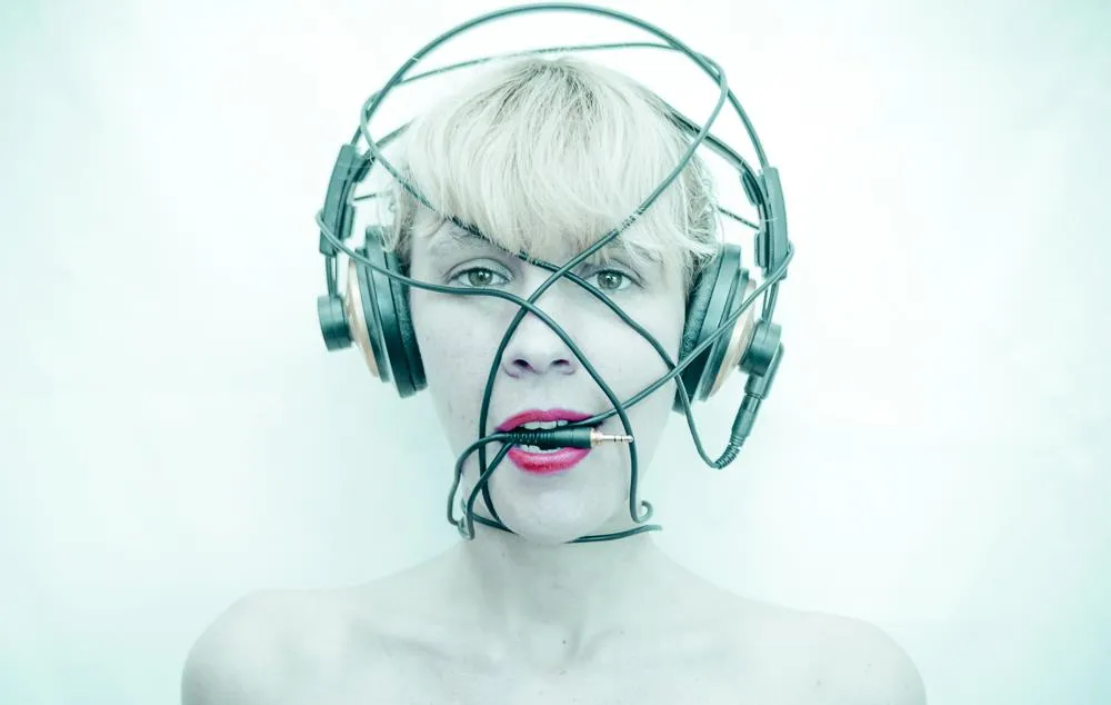 Emeraldia, headphones and cables wrapped around her face, a jack between her lips