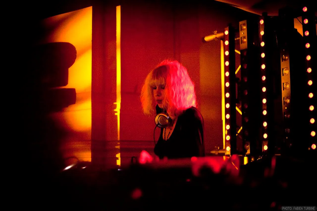 Emeraldia at the decks, headphones around her neck, in red light